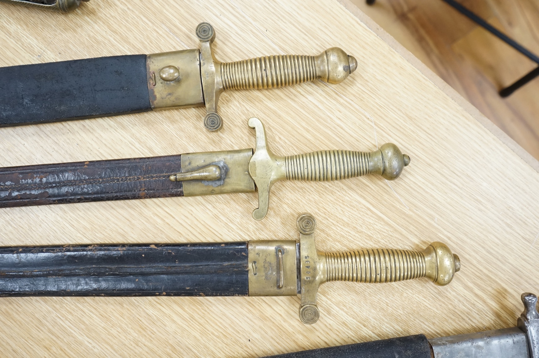 Three Continental infantry officer’s sidearms briquette, the first stamped Paris, in its brass mounted leather scabbard, another similar with sawback blade (illegible stamp), and another similar with thin blade, stamped